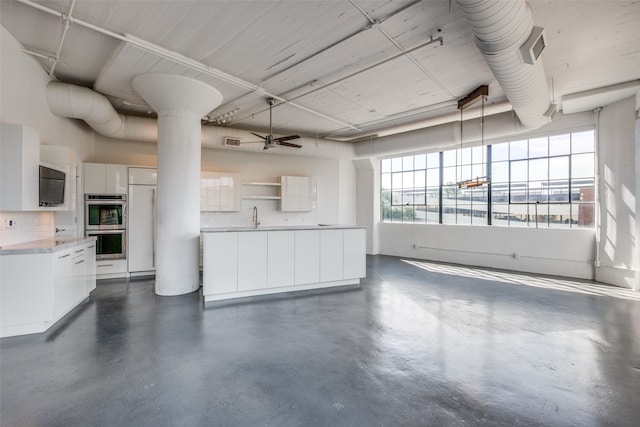 unfurnished living room with a high ceiling, ceiling fan, a healthy amount of sunlight, and sink