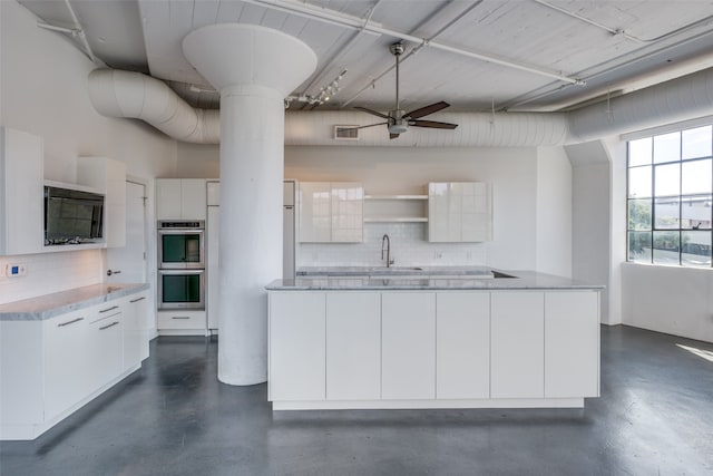 kitchen with ceiling fan, white cabinetry, backsplash, and double oven