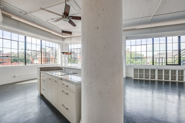 kitchen with black electric stovetop, light stone counters, white cabinetry, and a wealth of natural light