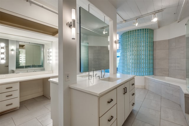 bathroom with tile patterned flooring, vanity, rail lighting, and a relaxing tiled tub