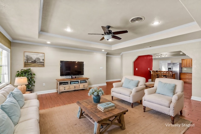 living room with ornamental molding, a raised ceiling, and light wood-type flooring