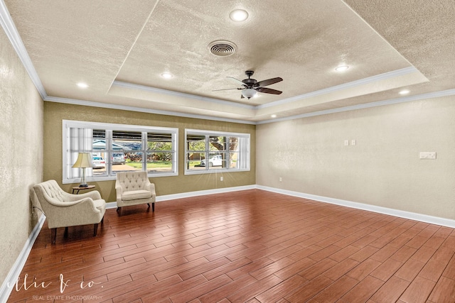 unfurnished room featuring a textured ceiling, a tray ceiling, wood finished floors, and visible vents