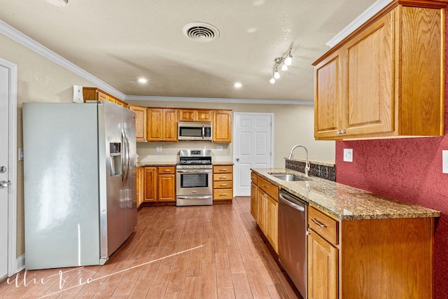 kitchen featuring sink, appliances with stainless steel finishes, light stone counters, ornamental molding, and light wood-type flooring