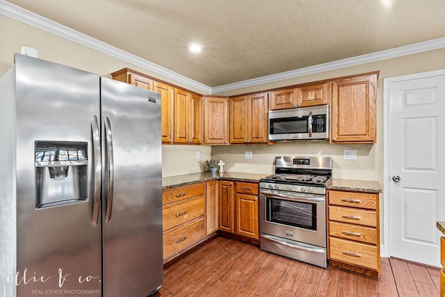 kitchen with crown molding, dark stone countertops, stainless steel appliances, and dark wood finished floors