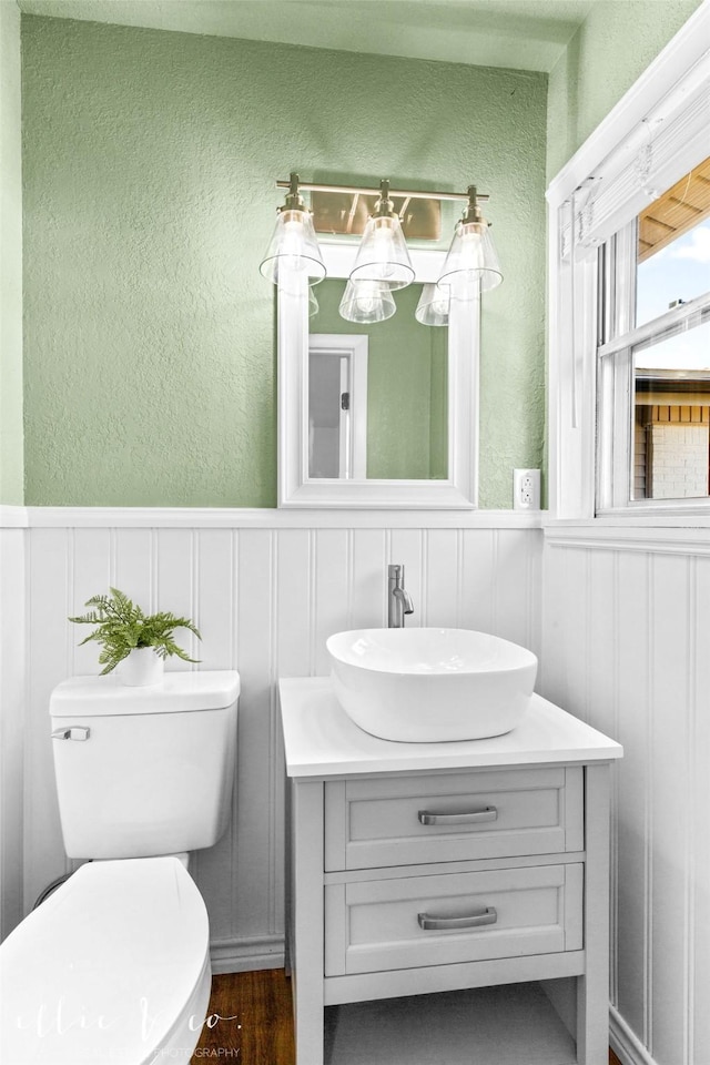 bathroom featuring wainscoting, a textured wall, vanity, and toilet