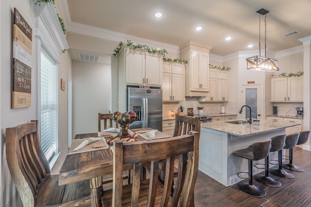 kitchen featuring light stone countertops, sink, stainless steel fridge with ice dispenser, dark hardwood / wood-style flooring, and a center island with sink