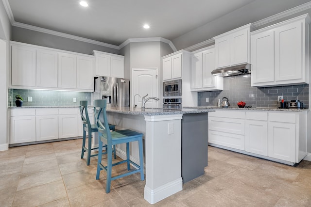 kitchen featuring a kitchen island with sink, appliances with stainless steel finishes, tasteful backsplash, a kitchen bar, and white cabinetry