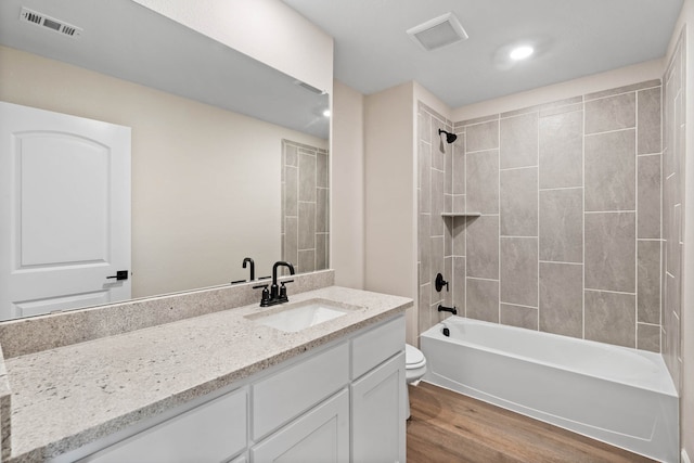 full bathroom featuring hardwood / wood-style floors, tiled shower / bath combo, toilet, and vanity