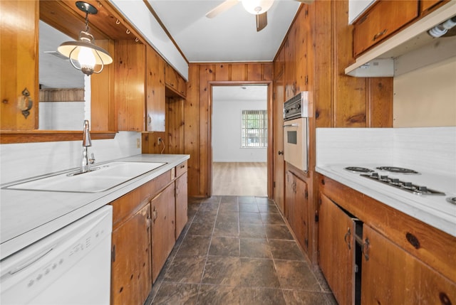 kitchen featuring ceiling fan, sink, hanging light fixtures, white appliances, and wooden walls