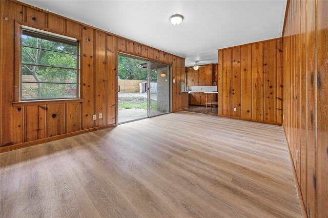 unfurnished living room with wooden walls, light hardwood / wood-style flooring, and ceiling fan