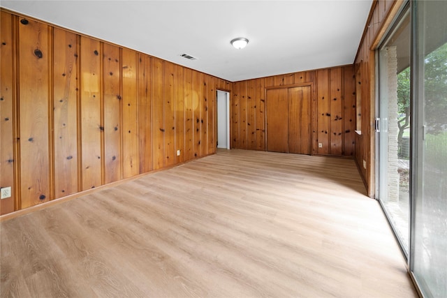 empty room with light wood-type flooring and wooden walls