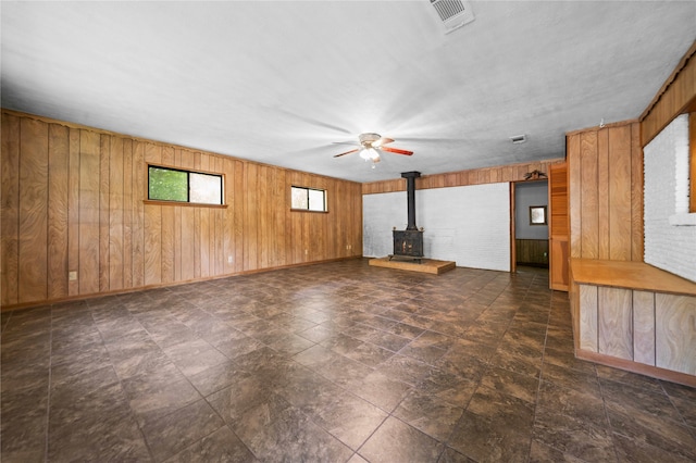 unfurnished living room with ceiling fan, wood walls, and a wood stove