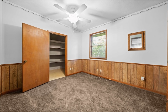 unfurnished bedroom with dark colored carpet, ceiling fan, wooden walls, and a closet