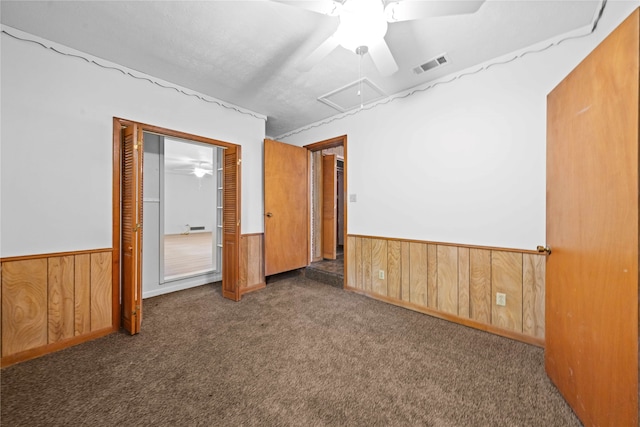 unfurnished room with wood walls, ceiling fan, and dark colored carpet