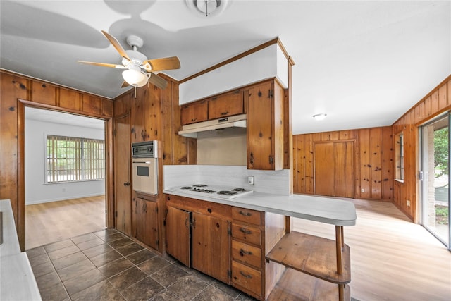 kitchen with ornamental molding, white appliances, ceiling fan, wooden walls, and dark hardwood / wood-style floors