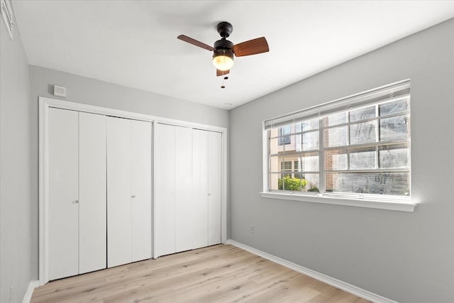 unfurnished bedroom with ceiling fan, light wood-type flooring, and multiple closets