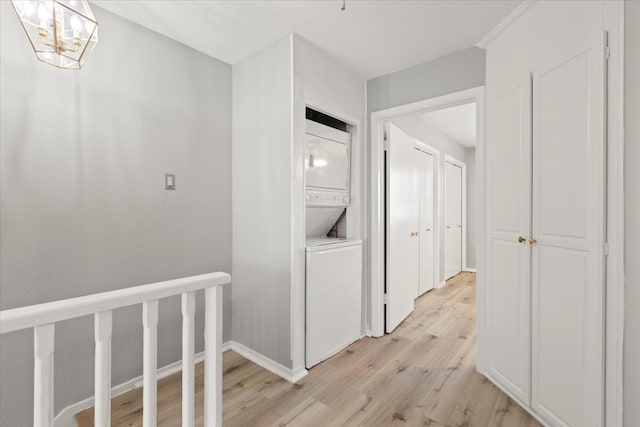 hallway with light wood-type flooring, stacked washer / dryer, and a notable chandelier