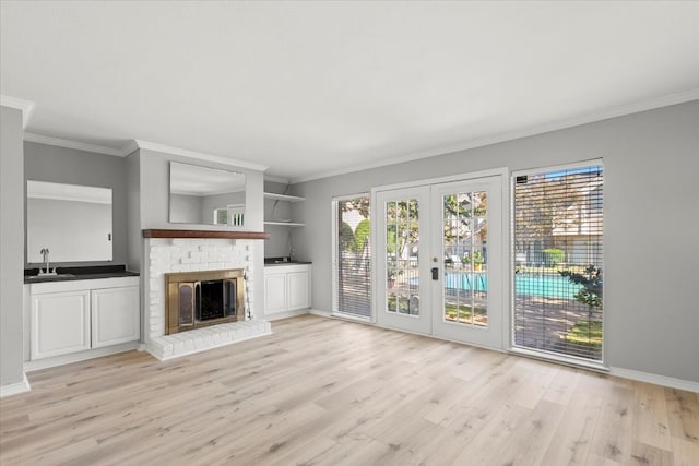 unfurnished living room featuring french doors, sink, a brick fireplace, light hardwood / wood-style flooring, and crown molding