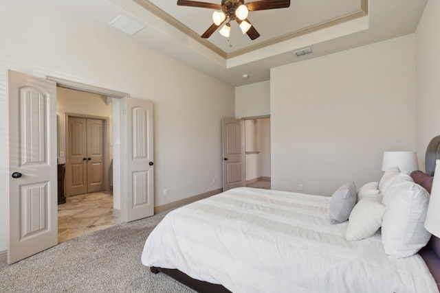 carpeted bedroom with visible vents, baseboards, ceiling fan, ornamental molding, and a tray ceiling