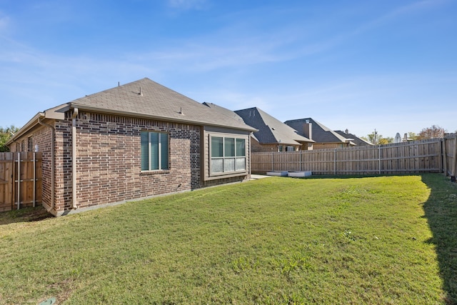 back of house featuring a yard, brick siding, a shingled roof, and a fenced backyard