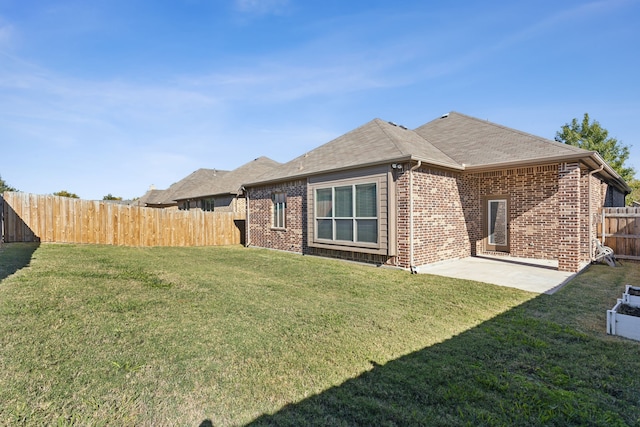 rear view of house with brick siding, a yard, a patio, a shingled roof, and a fenced backyard