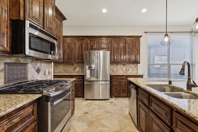 kitchen with dark brown cabinetry, appliances with stainless steel finishes, decorative light fixtures, light stone countertops, and a sink