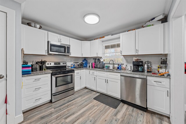 kitchen featuring light stone countertops, appliances with stainless steel finishes, sink, light hardwood / wood-style flooring, and white cabinets