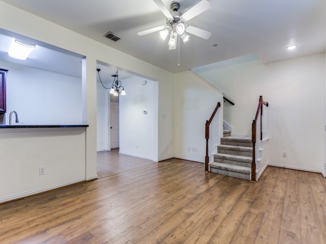 unfurnished living room with wood-type flooring, ceiling fan with notable chandelier, and sink