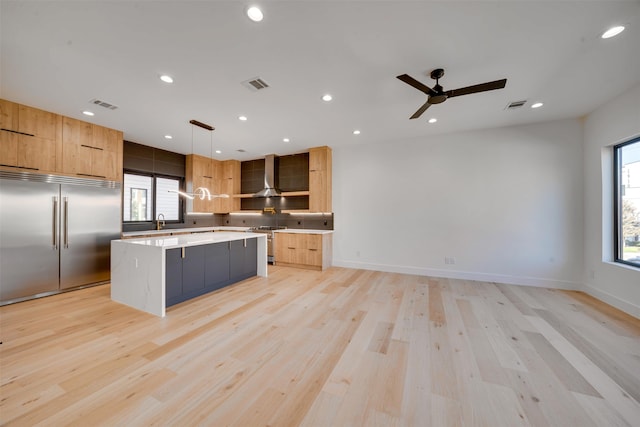 kitchen featuring pendant lighting, wall chimney range hood, light hardwood / wood-style floors, a kitchen island, and stainless steel appliances