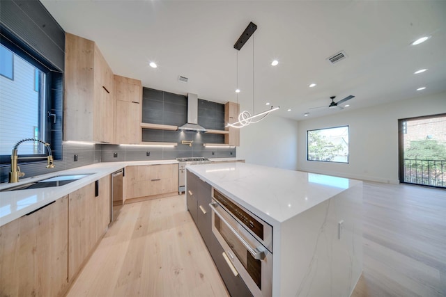 kitchen featuring sink, wall chimney exhaust hood, light stone countertops, decorative light fixtures, and a kitchen island