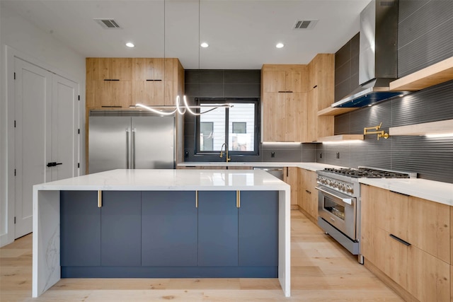 kitchen with a center island, light hardwood / wood-style floors, high end appliances, and wall chimney exhaust hood