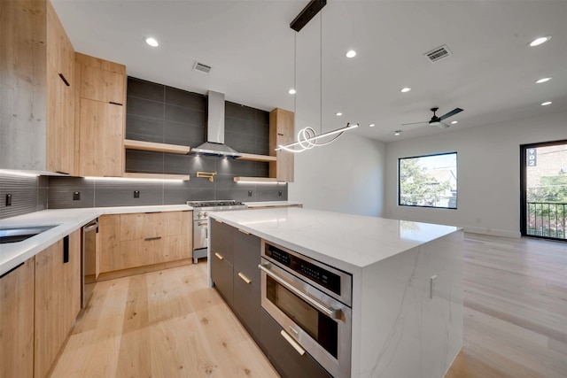 kitchen featuring appliances with stainless steel finishes, light wood-type flooring, ceiling fan, decorative light fixtures, and a kitchen island