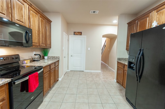 kitchen with black appliances, light stone counters, and light tile patterned floors