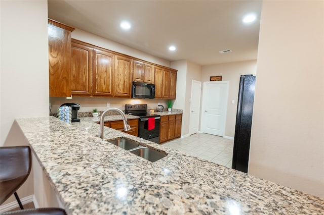 kitchen with a kitchen bar, light stone countertops, sink, black appliances, and light tile patterned floors