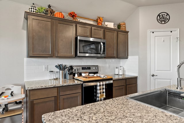 kitchen with sink, light stone counters, backsplash, dark brown cabinets, and appliances with stainless steel finishes