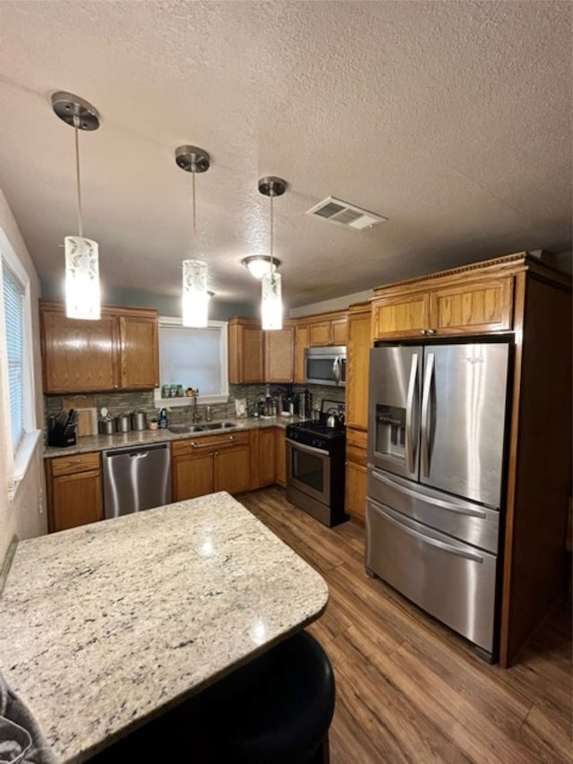 kitchen featuring wood-type flooring, stainless steel appliances, hanging light fixtures, and sink