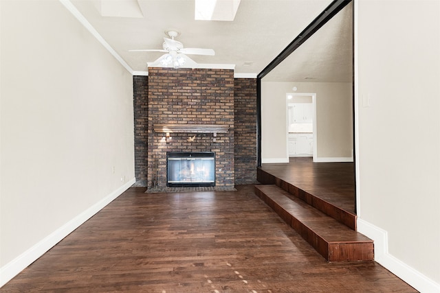 unfurnished living room featuring a skylight, ceiling fan, dark hardwood / wood-style floors, a fireplace, and ornamental molding