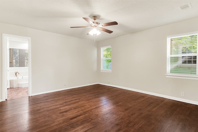 unfurnished room featuring a textured ceiling, ceiling fan, dark wood-type flooring, and a wealth of natural light