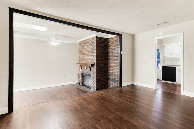 unfurnished living room with ceiling fan, dark hardwood / wood-style flooring, a textured ceiling, and a brick fireplace