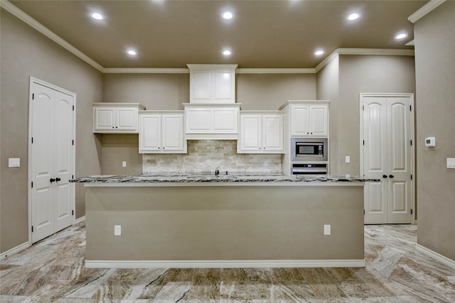 kitchen featuring stainless steel appliances, light stone counters, backsplash, a center island with sink, and white cabinets