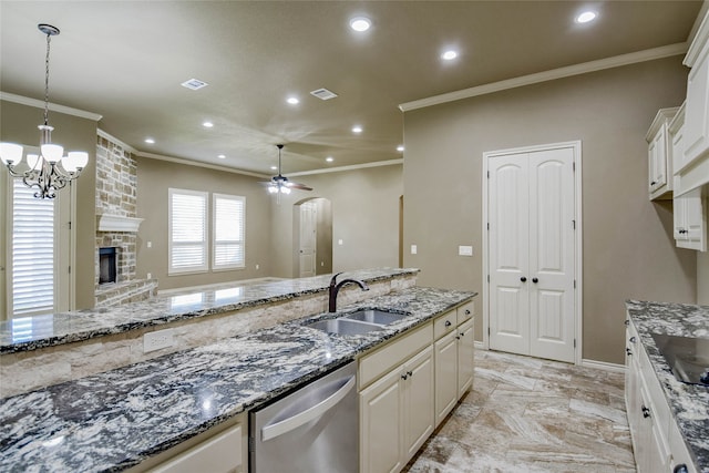 kitchen with sink, stainless steel dishwasher, dark stone countertops, a fireplace, and white cabinets