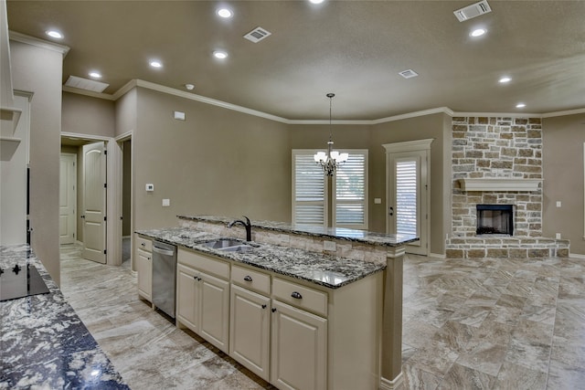 kitchen featuring sink, a fireplace, an island with sink, decorative light fixtures, and light stone counters