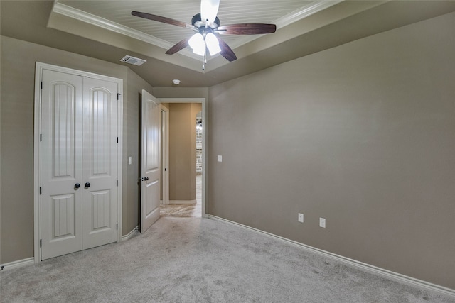 unfurnished bedroom featuring ceiling fan, a tray ceiling, light carpet, a closet, and ornamental molding