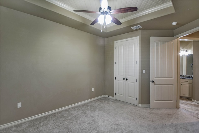 unfurnished bedroom with ceiling fan, crown molding, light colored carpet, a tray ceiling, and a closet