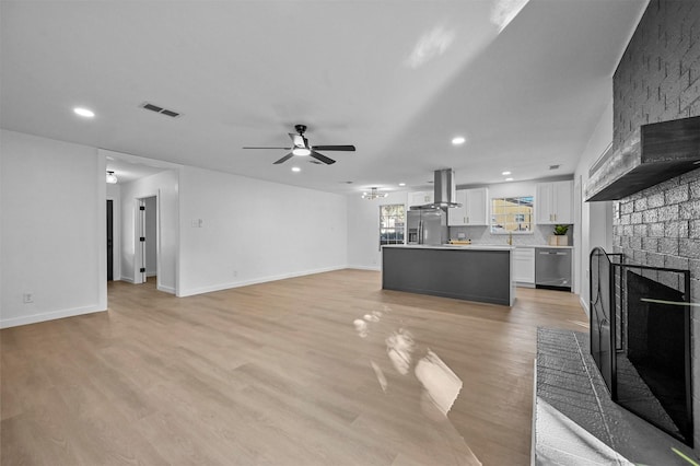 unfurnished living room with ceiling fan, a fireplace, and light hardwood / wood-style floors