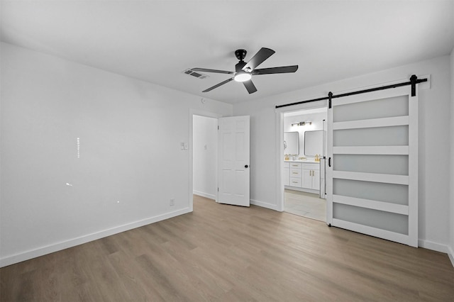 unfurnished bedroom featuring ensuite bath, light hardwood / wood-style flooring, a barn door, and ceiling fan