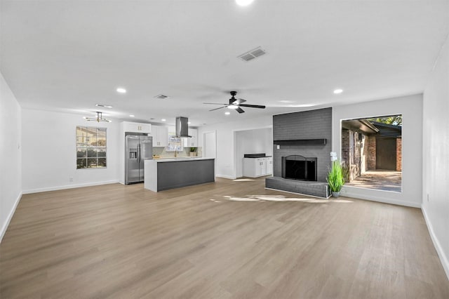 unfurnished living room with a brick fireplace, sink, ceiling fan, and light hardwood / wood-style flooring