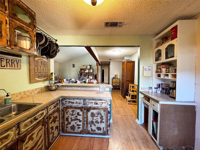 kitchen with lofted ceiling, sink, a textured ceiling, kitchen peninsula, and light hardwood / wood-style floors