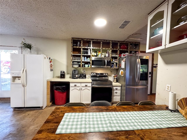 kitchen with appliances with stainless steel finishes, a textured ceiling, concrete floors, and white cabinets