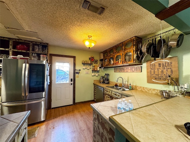 kitchen featuring dishwashing machine, sink, stainless steel refrigerator, hardwood / wood-style floors, and tile countertops